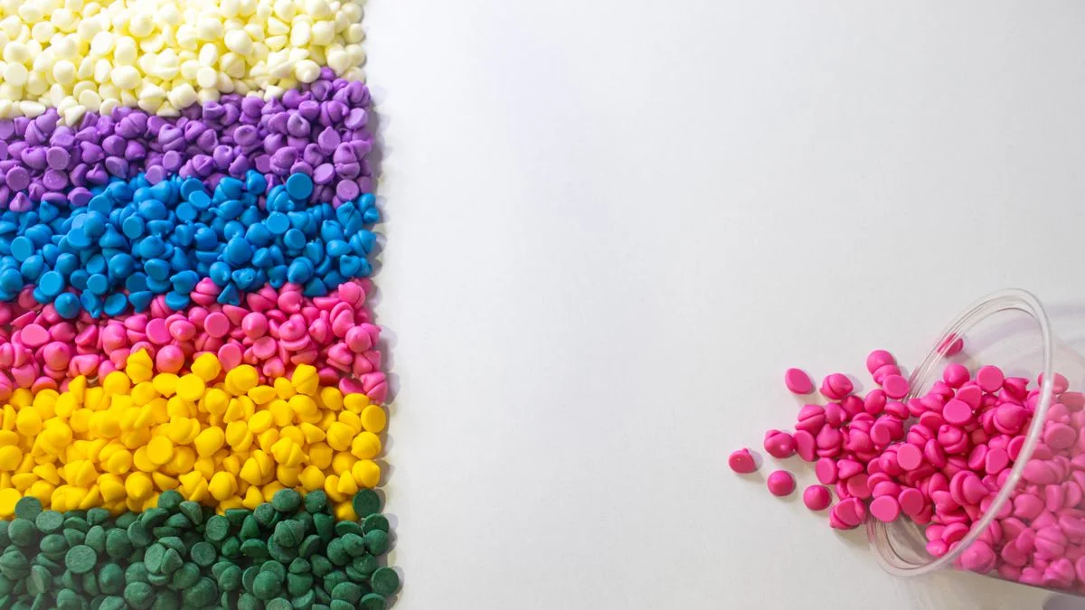 Filas de gránulos de masterbatch de plástico de colores derramándose de un recipiente transparente. - Pexels

