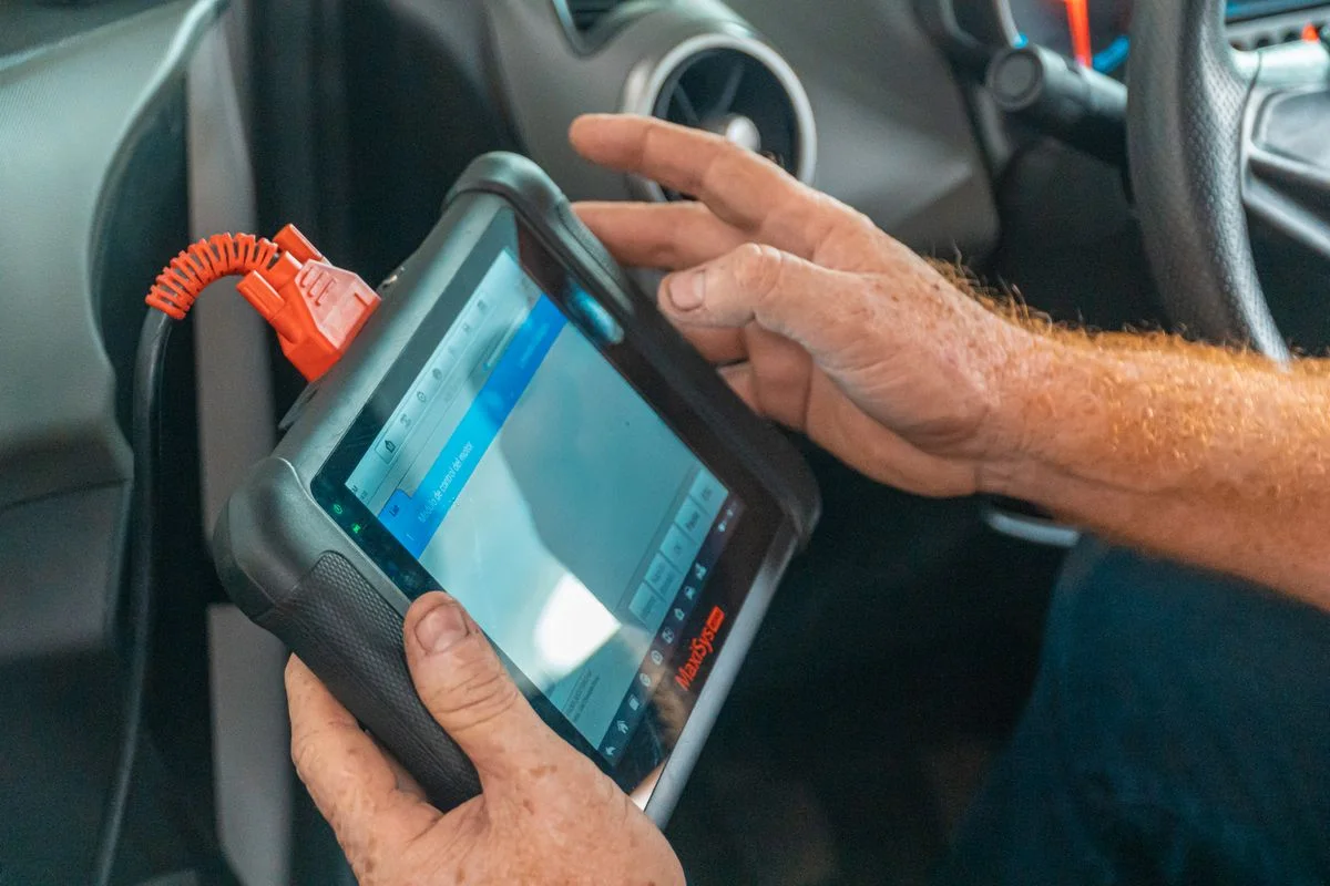 整備ダッシュボード監視のために車両システムに接続されたハンドヘルド診断タブレットを使用する技術者。 - Pexels