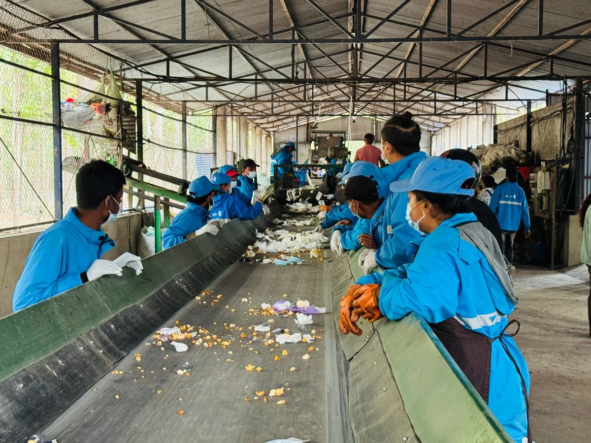 Workers manually sort mixed recyclable plastics along a conveyor belt. - Pexels

