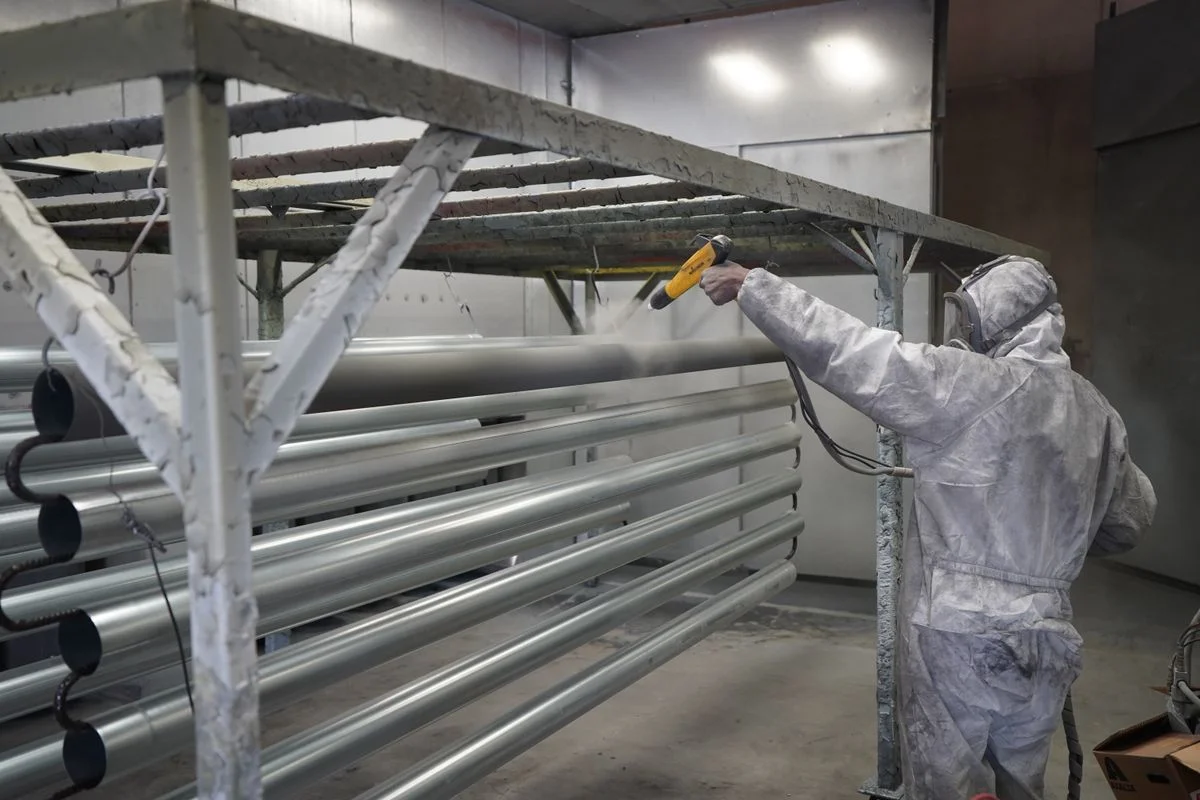 El operador aplica recubrimiento industrial en polvo a tubos metálicos en una cabina de pulverización. - Pexels

