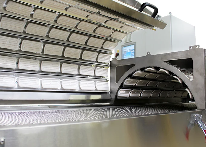 Preformas de PET dispuestas en filas sobre una cinta transportadora de acero inoxidable dentro de una máquina de calentamiento industrial - CERAMICX LTD. | Cpsemarketplace

