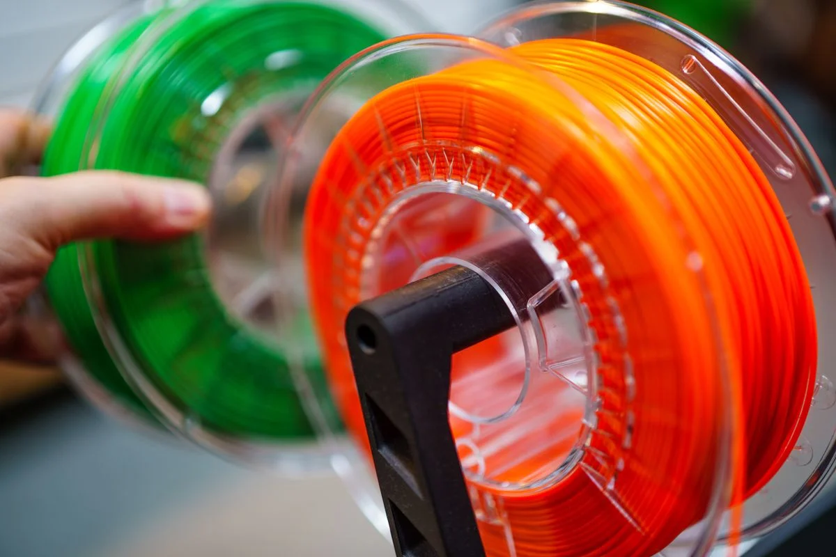 Carretes de filamento de impresión 3D verde y naranja enrollados ordenadamente sobre un soporte negro. - Pexels

